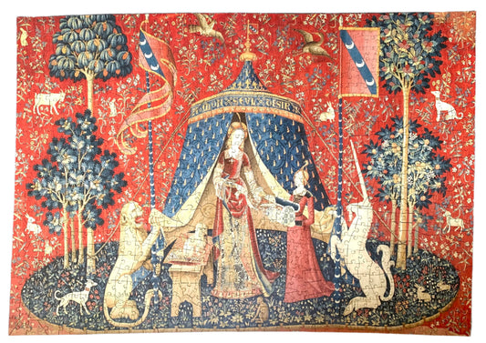 A completed wooden jigsaw puzzle depicting a medieval-style tapestry scene with a figure, animals, and decorative elements in red, blue, and natural wood colors.
Photo by Karen King [image_link]