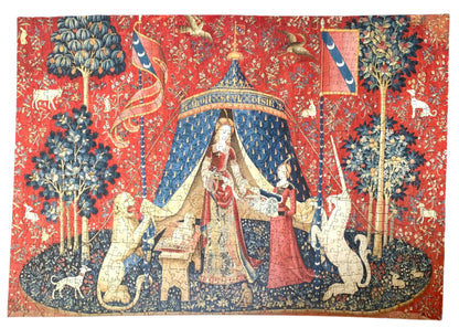 A completed wooden jigsaw puzzle depicting a medieval-style tapestry scene with a figure, animals, and decorative elements in red, blue, and natural wood colors.
Photo by Karen King [additional_image_link]
