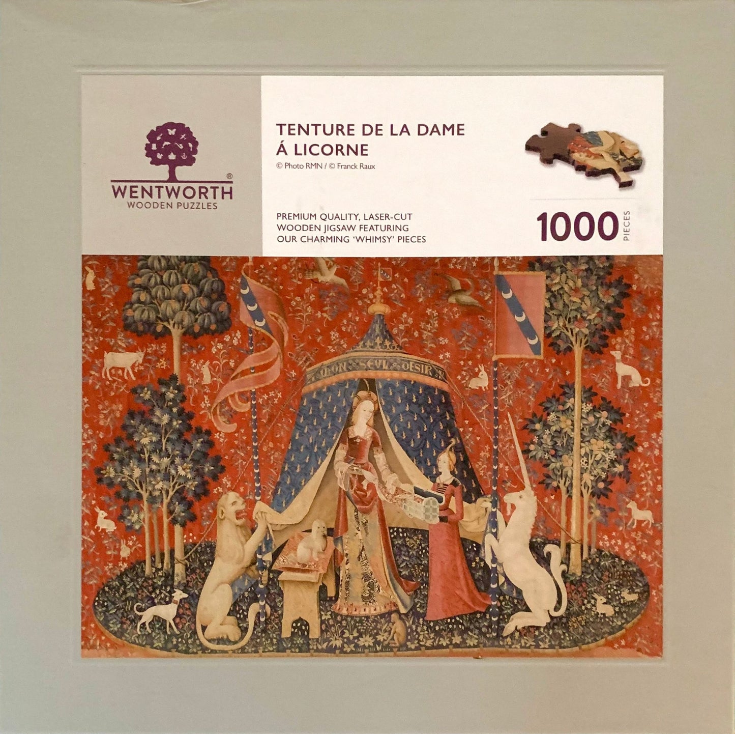 A completed wooden jigsaw puzzle depicting a medieval-style tapestry scene with a figure, animals, and decorative elements in red, blue, and natural wood colors.
Photo by Karen King [additional_image_link]