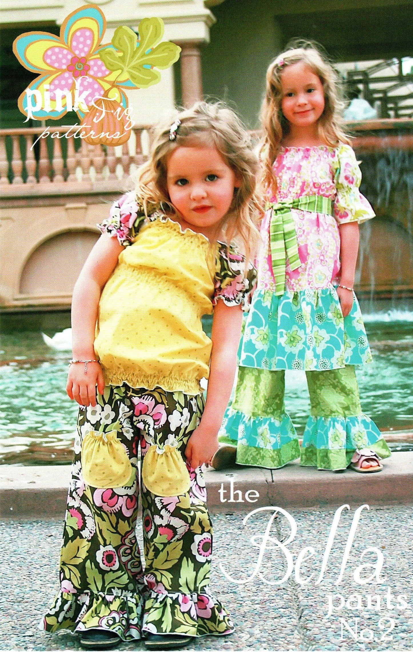 Two young girls modeling floral ruffled pants and matching tops in an outdoor setting with a fountain in the background. The image features a 'pink patterns' logo in the top left and 'the Bella pants No. 2
Photo by Pink Fig Patterns [additional_image_link]