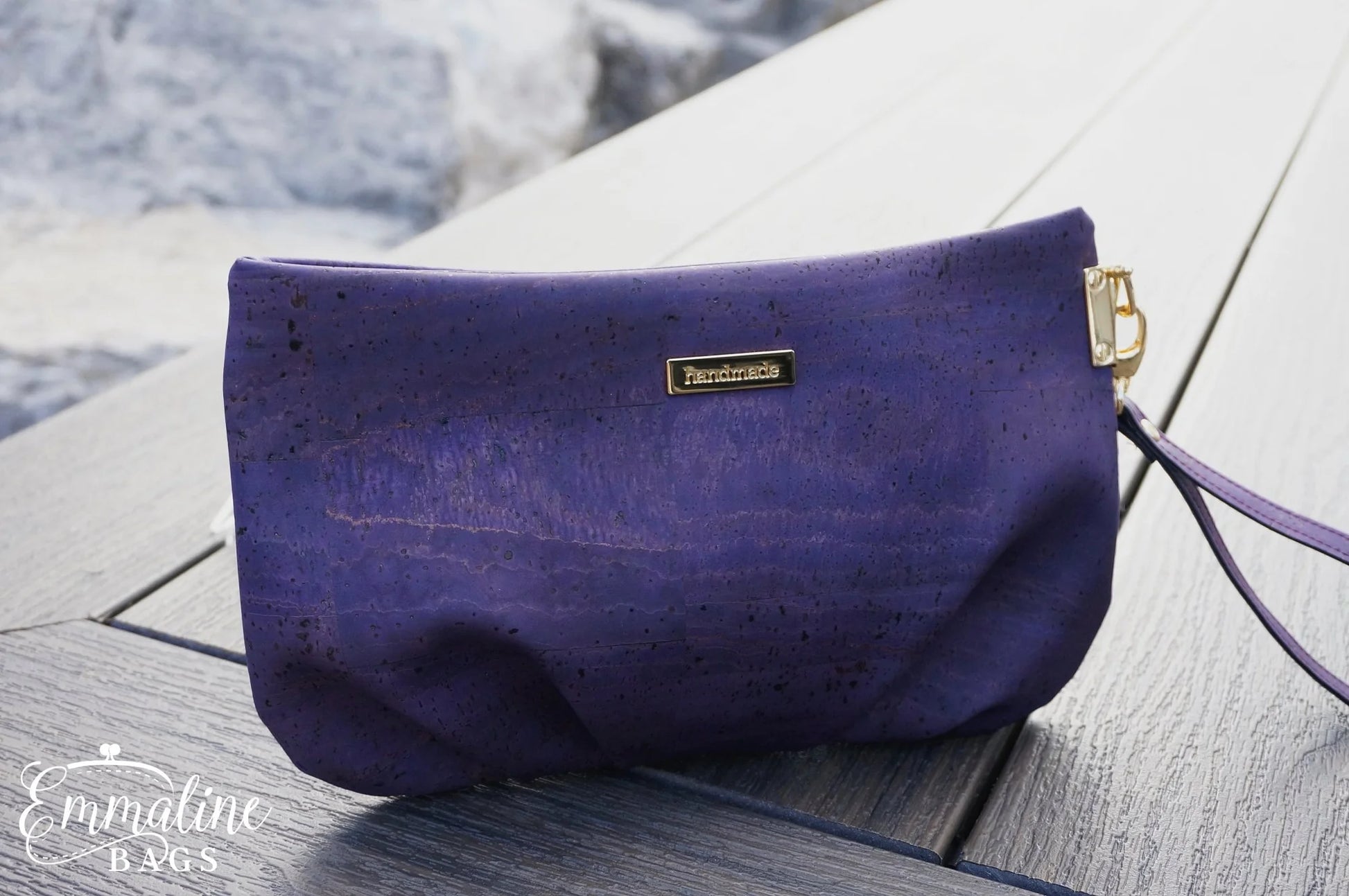 Purple clutch bag with gold zipper on a wooden surface near water.
Photo by Emmaline Bags [additional_image_link]