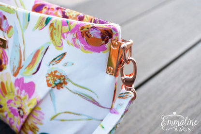 Floral-patterned bag with a gold clasp on a wooden surface, featuring the brand 'Emmaline Bags'.
Photo by Emmaline Bags [additional_image_link]
