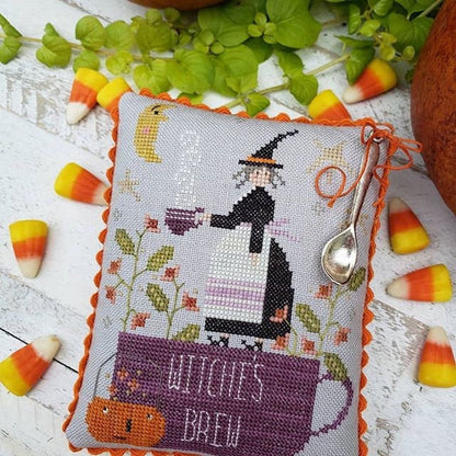 Cross-stitched pillow with witch design and 'Witch's Brew' text, surrounded by candy corn and leaves on a wooden surface.
[additional_image_link]