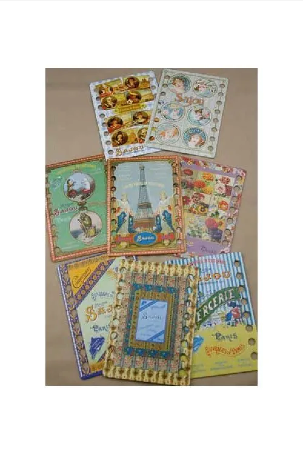 A collection of vintage French thread organizers and small illustrated cards arranged on a beige surface. The organizers feature colorful depictions of Parisian scenes, including the Eiffel Tower, street signs, and characters, with some cards showing small printed illustrations and one card featuring a central blue panel.
Photo by Sajou.fr [additional_image_link]