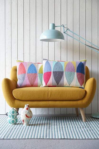 A yellow upholstered loveseat with two colorful quilted pillows, set against a white wood-paneled wall with a light blue floor lamp and striped rug.
Photo by Tildafabrics.com [additional_image_link]