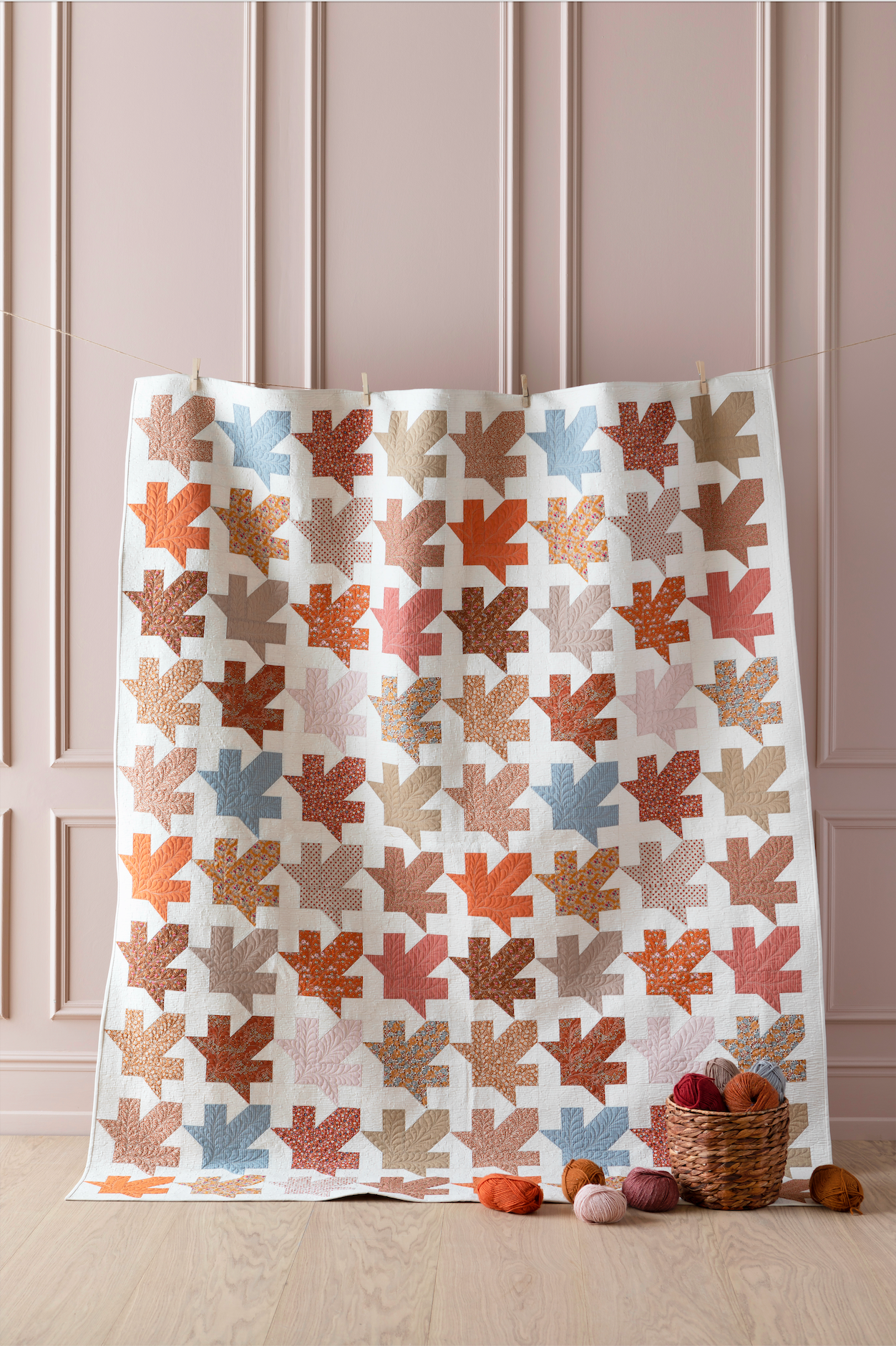 A quilt with a maple leaf pattern featuring various shades of autumn such as brown, orange, and yellow, displayed on a hanger.
Photo by Tildafabrics.com [image_link]