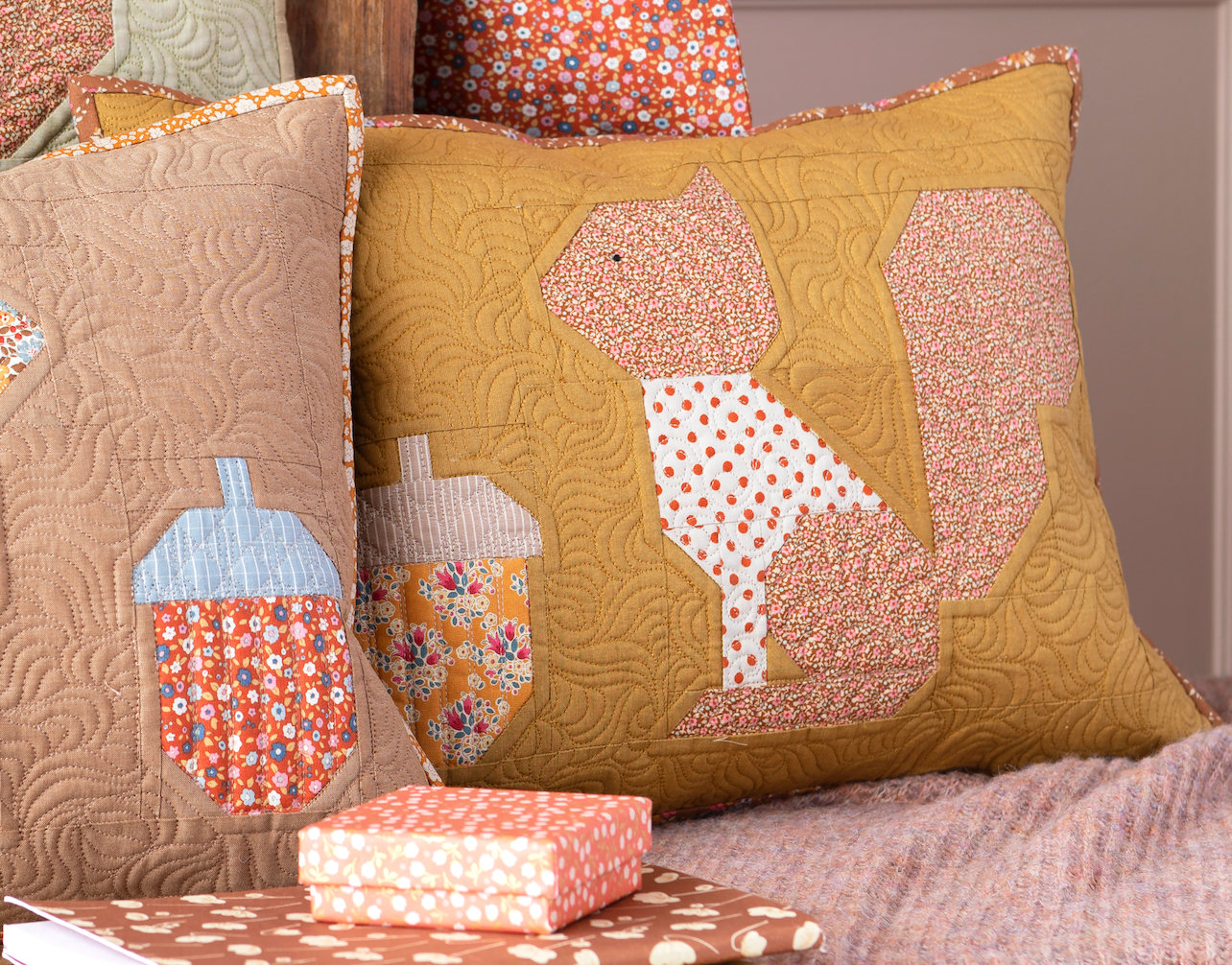 Two decorative quilted throw pillows displayed together on a bed or sofa. The larger pillow is mustard yellow with a squirrel applique made of pink, peach, and white polka-dot fabric.
Photo by Tildafabrics.com [additional_image_link]