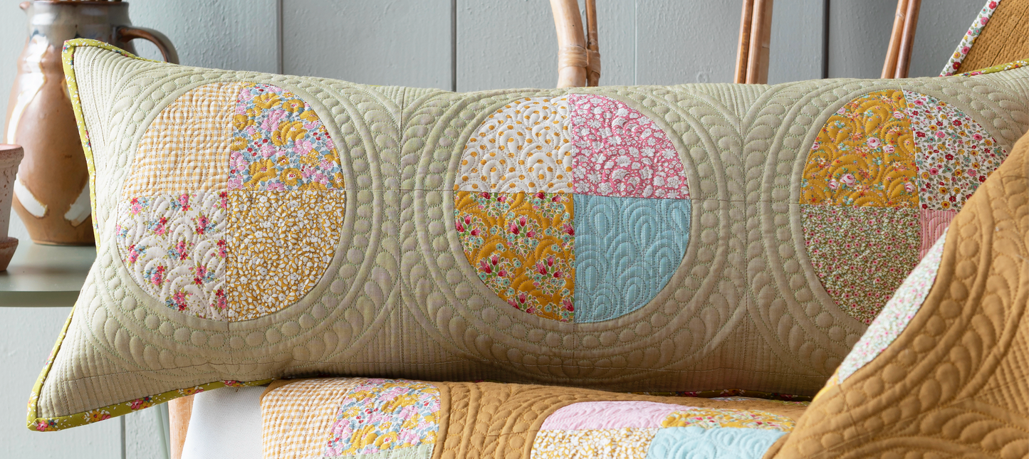A long rectangular quilted lumbar pillow with circular patchwork panel eggs in beige, yellow, pink, and light blue, resting on a matching quilted sofa.
Photo by Tildafabrics.com [image_link]