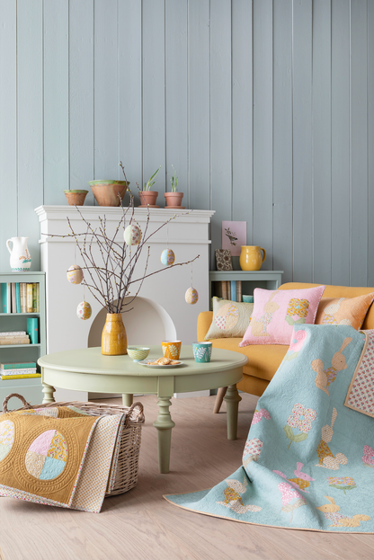 A styled living room scene with a light blue paneled wall, a yellow-orange armchair, a pale green round coffee table, and a pastel blue throw blanket draped over the chair. The blanket features a bunny and floral pattern.
Photo by Tildafabrics.com [additional_image_link]