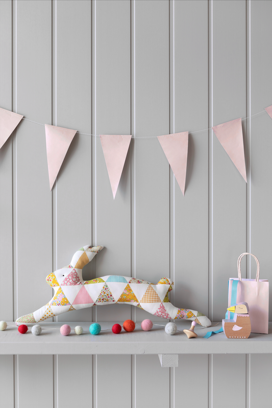 A finished patchwork hare kit displayed on a shelf with Easter-themed decorations and a striped background.
Photo by Tildafabrics.com [image_link]