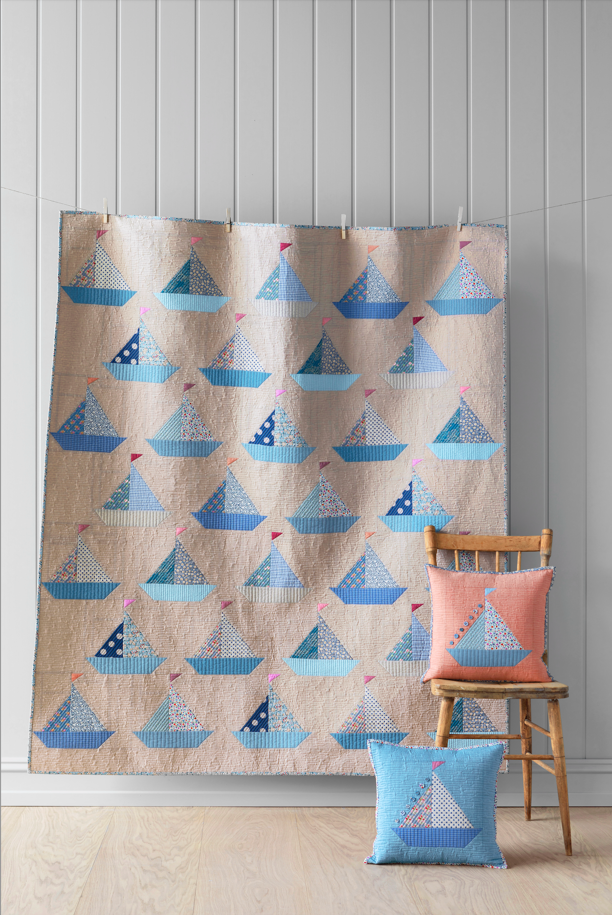 A completed sailboat quilt displayed on a wall with a chair and a cushion with a similar design in front, all arranged in a home setting.
Photo by Tildafabrics.com [image_link]