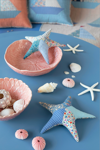 A styled tabletop scene with two fabric starfish decorations, pink ceramic bowls, seashells, and white starfish on a blue surface. No person or animal is present, and the image is a clean styled product presentation rather than a real environment-focused lifestyle shot, so Product/Packaging fits best.
Photo by Tildafabrics.com [additional_image_link]