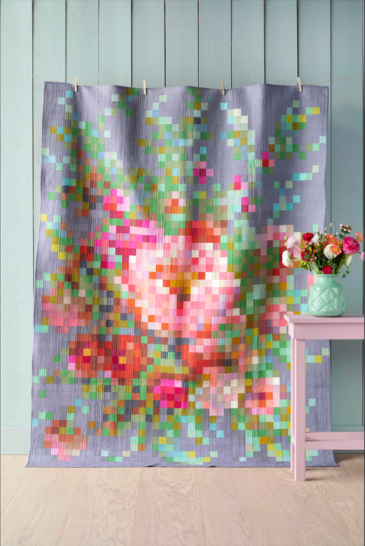 A fabric shower curtain with a colorful pixelated floral print hanging on a light blue paneled wall, with a small pink side table and vase of flowers to the right.
Photo by Tildafabrics.com [image_link]
