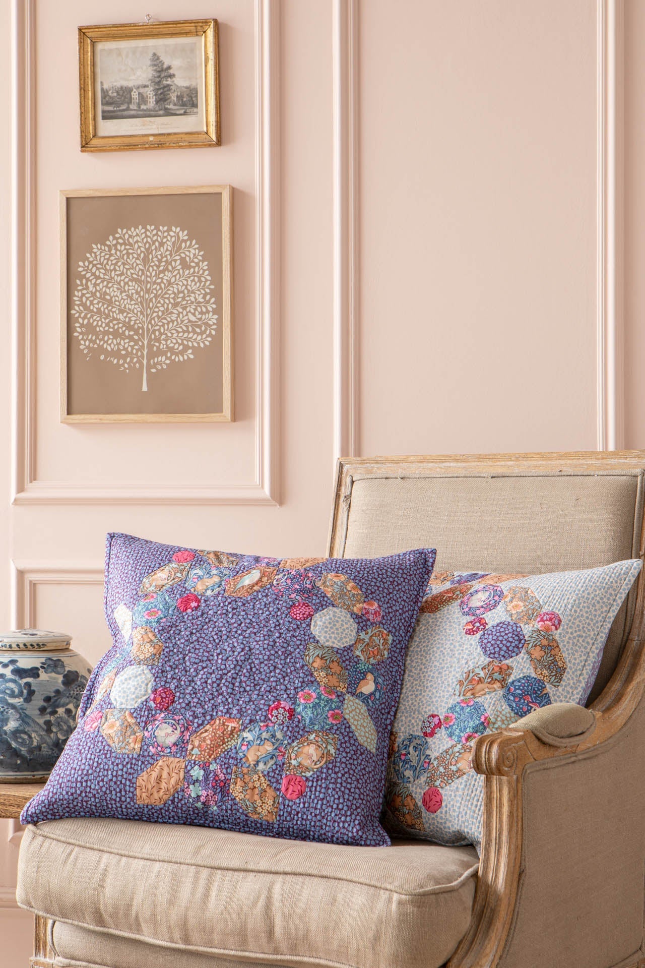 Two decorative throw pillows displayed on a beige upholstered armchair in a styled room setting with pink paneled walls and framed wall art.
Photo by Tildafabrics.com [additional_image_link]