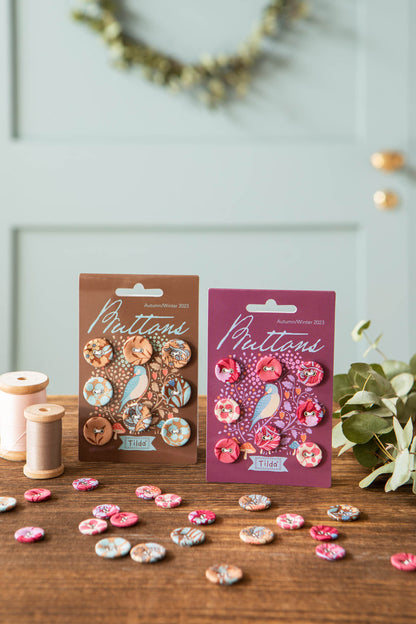 Two packages of Hibernation fabric buttons displayed on a wooden table, with loose buttons scattered around and sewing thread spools in the background.
Photo by Tildafabrics.com [additional_image_link]