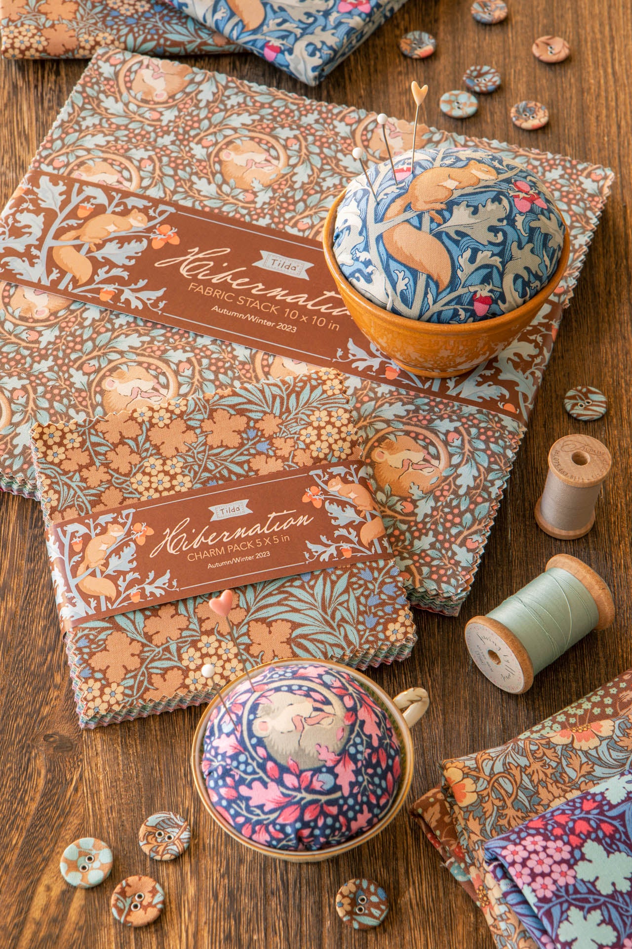 A styled flat-lay of Hibernation Fabric Stitch Kit in the 'Hikaru' pattern, showing the patterned fabric, a pincushion, a sewing needle case, thread spools, and buttons on a rustic wooden table.
Photo by Tildafabrics.com [additional_image_link]