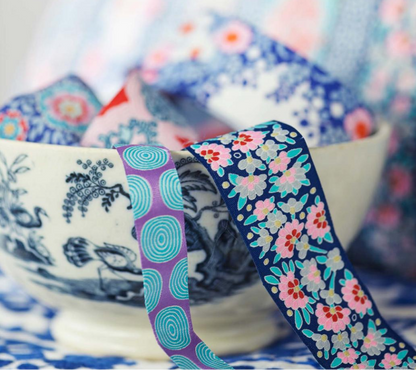 A bowl filled with colorful patterned ribbons, including floral and paisley designs in blue, pink, purple, and teal. The background shows a soft-focus view of matching patterned fabric.
Photo by Tildafabrics.com [additional_image_link]