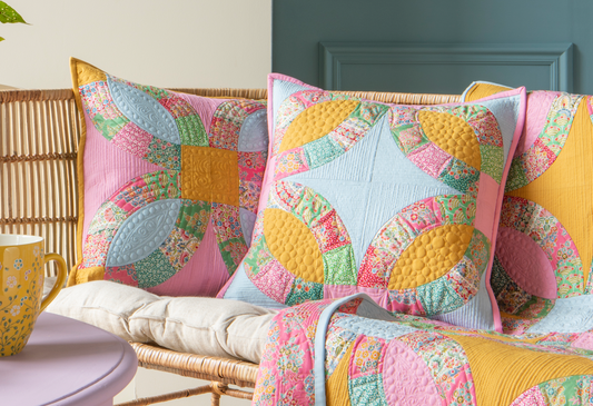 A styled interior scene showing a pastel quilted throw blanket and matching decorative pillows with a colorful butterfly patchwork pattern, arranged on a sofa in a room with blue paneled walls and a lavender side table.
Photo by Tildafabrics.com [image_link]