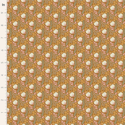 A close-up of a patterned fabric sample with a repeating floral design on a warm mustard background. The pattern includes cream flowers, pink leaves, and small blue-green dots, with a white measurement ruler along the left edge marked in inches.
Photo by Tildafabrics.com [image_link]