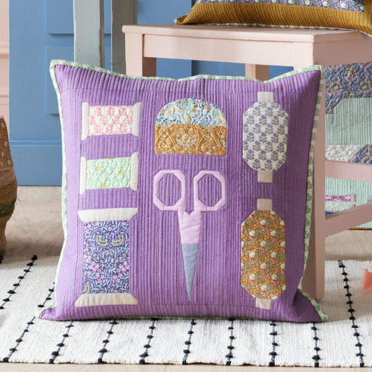 A pillow with a mix of fabric patches featuring various sewing-themed motifs such as scissors, pincushion, and cotton reels, on an eggplant background.
Photo by Tildafabrics.com [image_link]