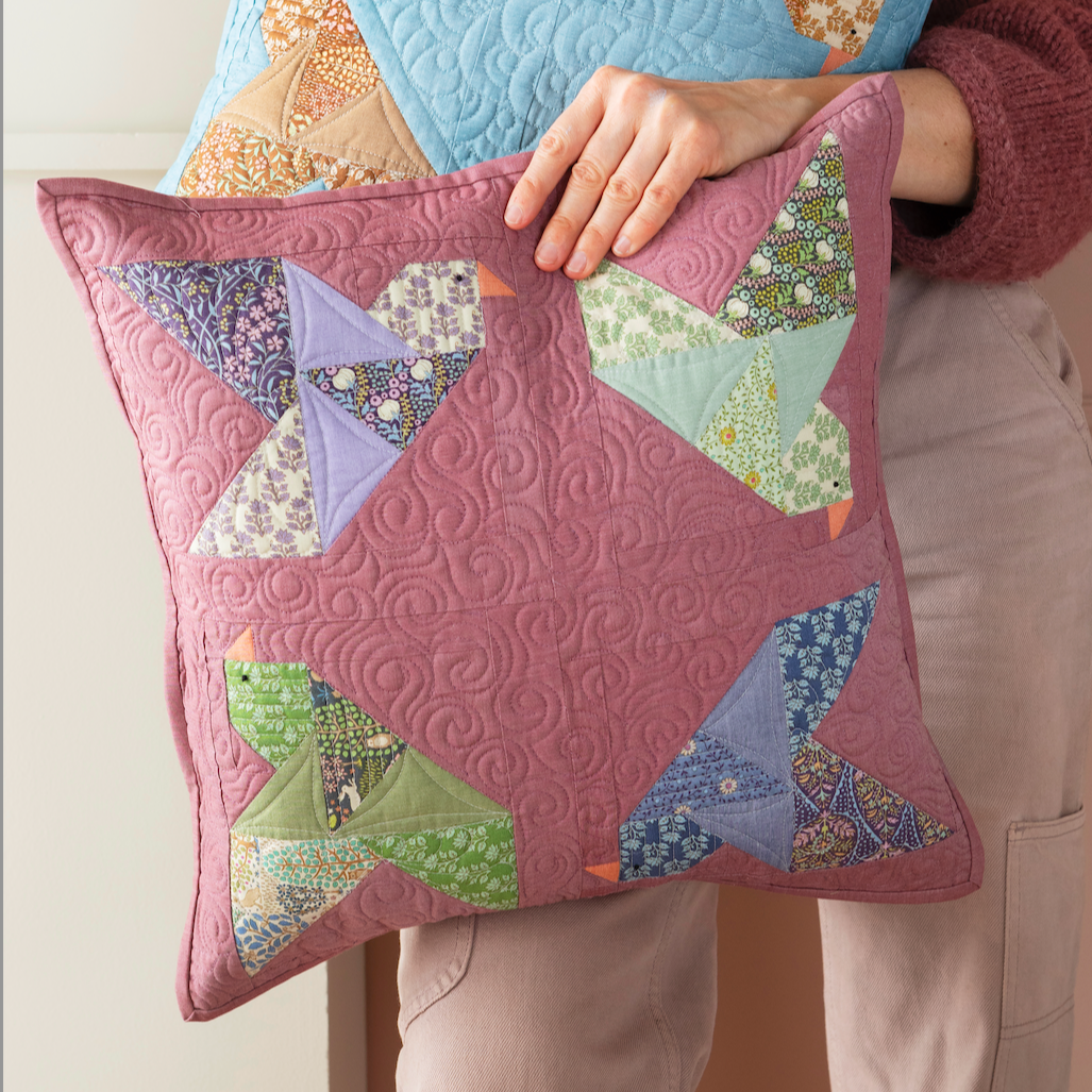 A woman a quilted square pillows with patchwork bird designs. The pillow is dusty pink.
Photo by Tildafabrics.com [image_link]