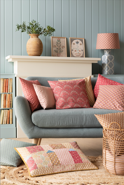 A quilt with a geometric pattern featuring small houses in warm colors, hanging on a wall with a blue wall panel and a small decorative pillow to the side.
Photo by Tildafabrics.com [additional_image_link]