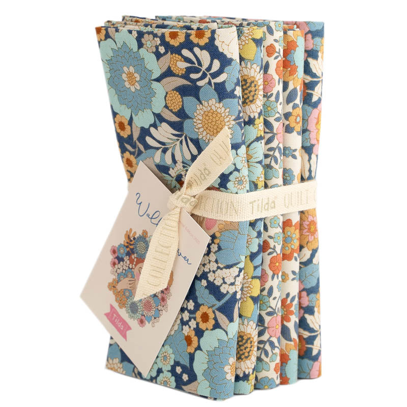 Five fat quarter bundles of Tilda Wallflower fabric with floral patterns in various blue colors, tied together with a tag displaying the brand and product name.
Photo by Tildafabrics.com [additional_image_link]