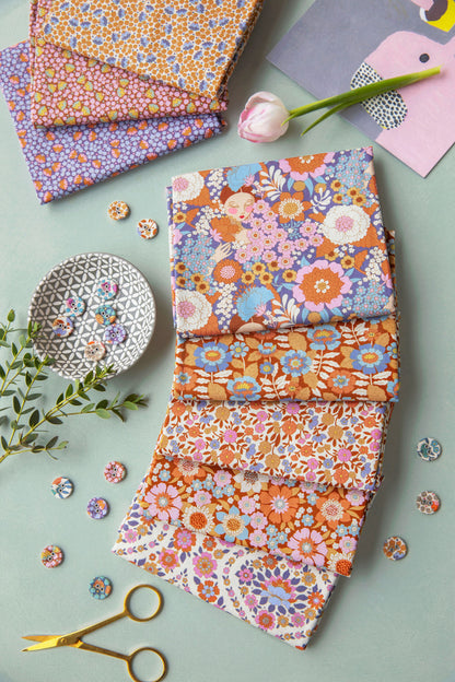 A styled flat-lay of several folded fabric pieces with colorful floral and paisley patterns, arranged on a pale blue-green surface with scissors, buttons, a tulip, and decorative paper props.
Photo by Tildafabrics.com [additional_image_link]
