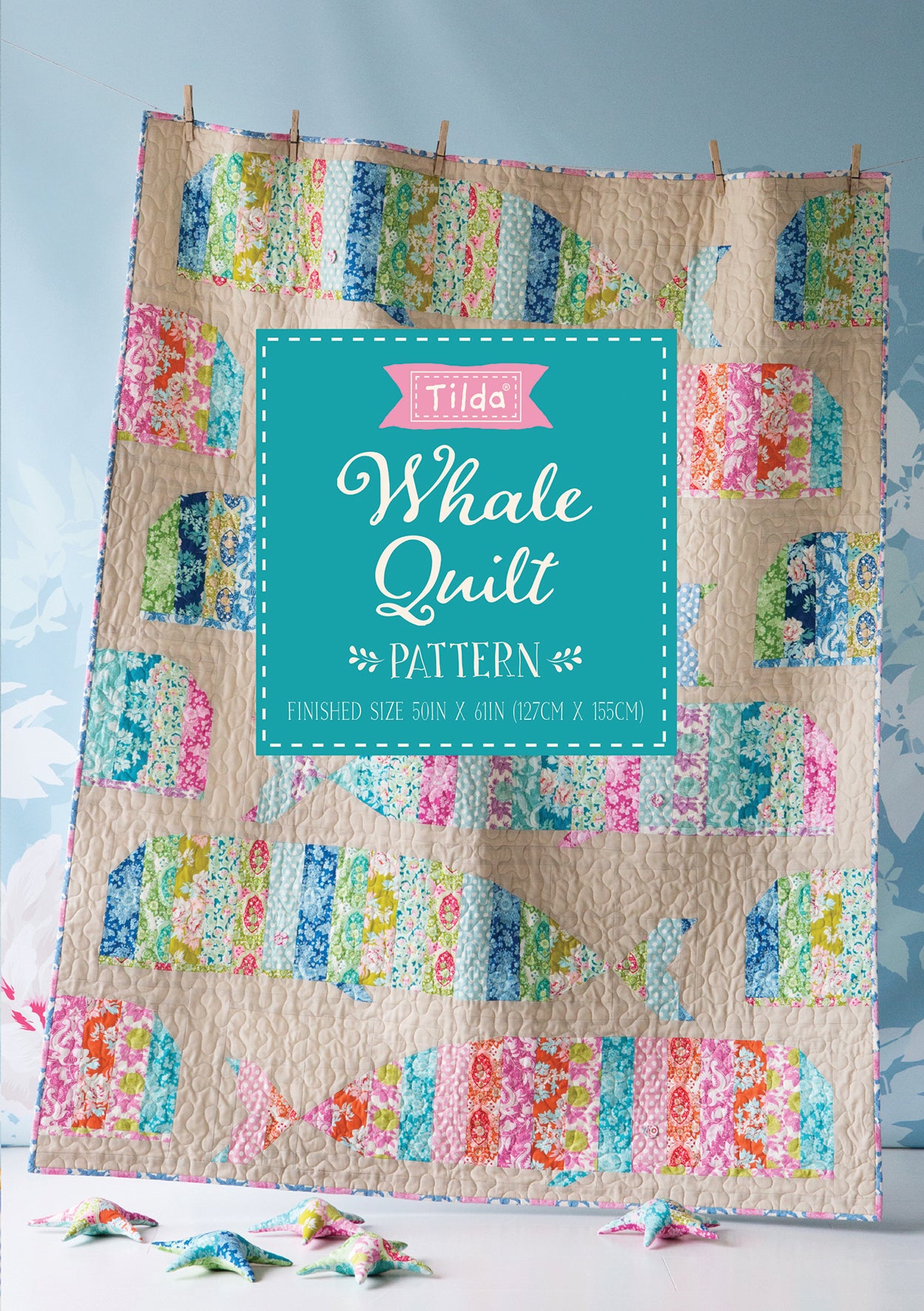 Whale quilt pattern cover featuring a colorful patchwork quilt with whale shapes on a beige background, with a large mint green central label reading 'Tilda Whale Quilt PATTERN'.
[additional_image_link]