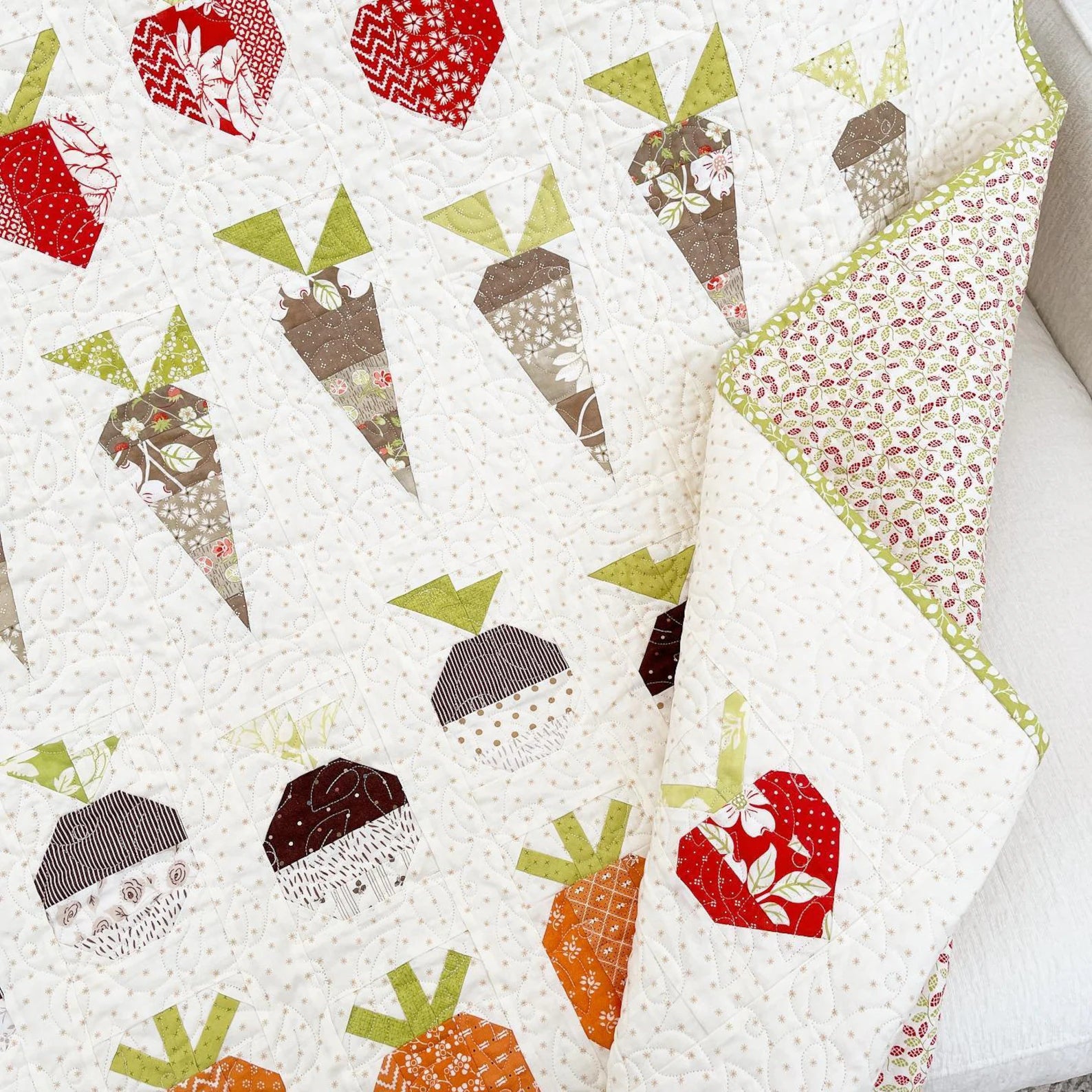 A close-up of a quilted baby blanket featuring a pattern of carrot-shaped appliques in red, orange, brown, and green on a white fabric background.
Photo by ThePatternBasket.com [additional_image_link]