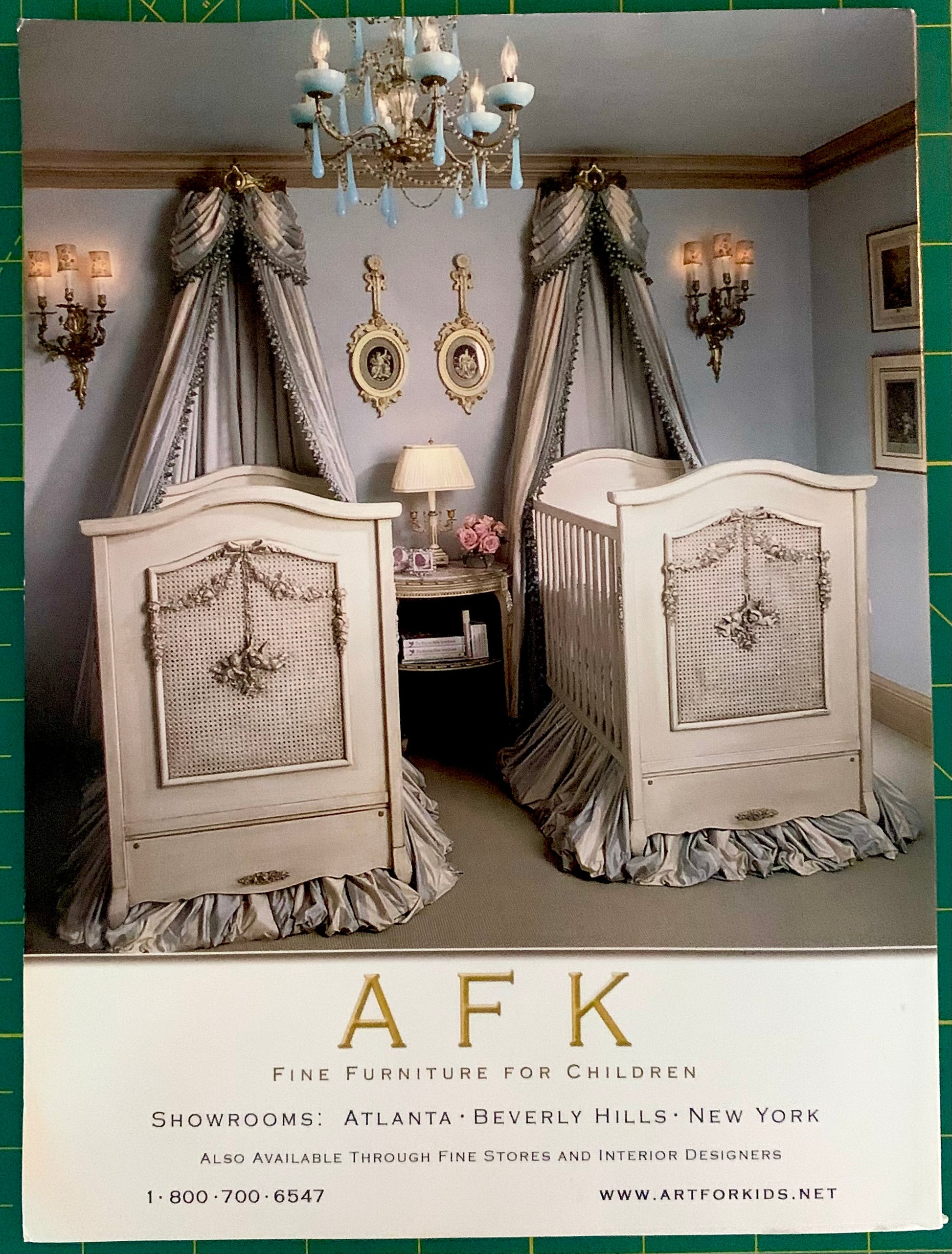 A vintage Art for Kids (AFK) fine furniture for children advertisement featuring two ornate white cribs with matching gray and white canopy curtains, set against a gray wall with decorative sconces and gold frames. The bottom of the ad features the AFK logo and contact information.
[additional_image_link]