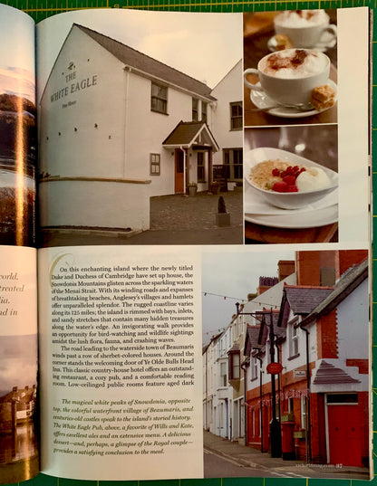 An open book spread showing a travel article about White Eagle in Scotland, with black-and-white and color photographs of a large white building, a red-and-white building, and a cup of cappuccino with a strawberry dessert.
[additional_image_link]