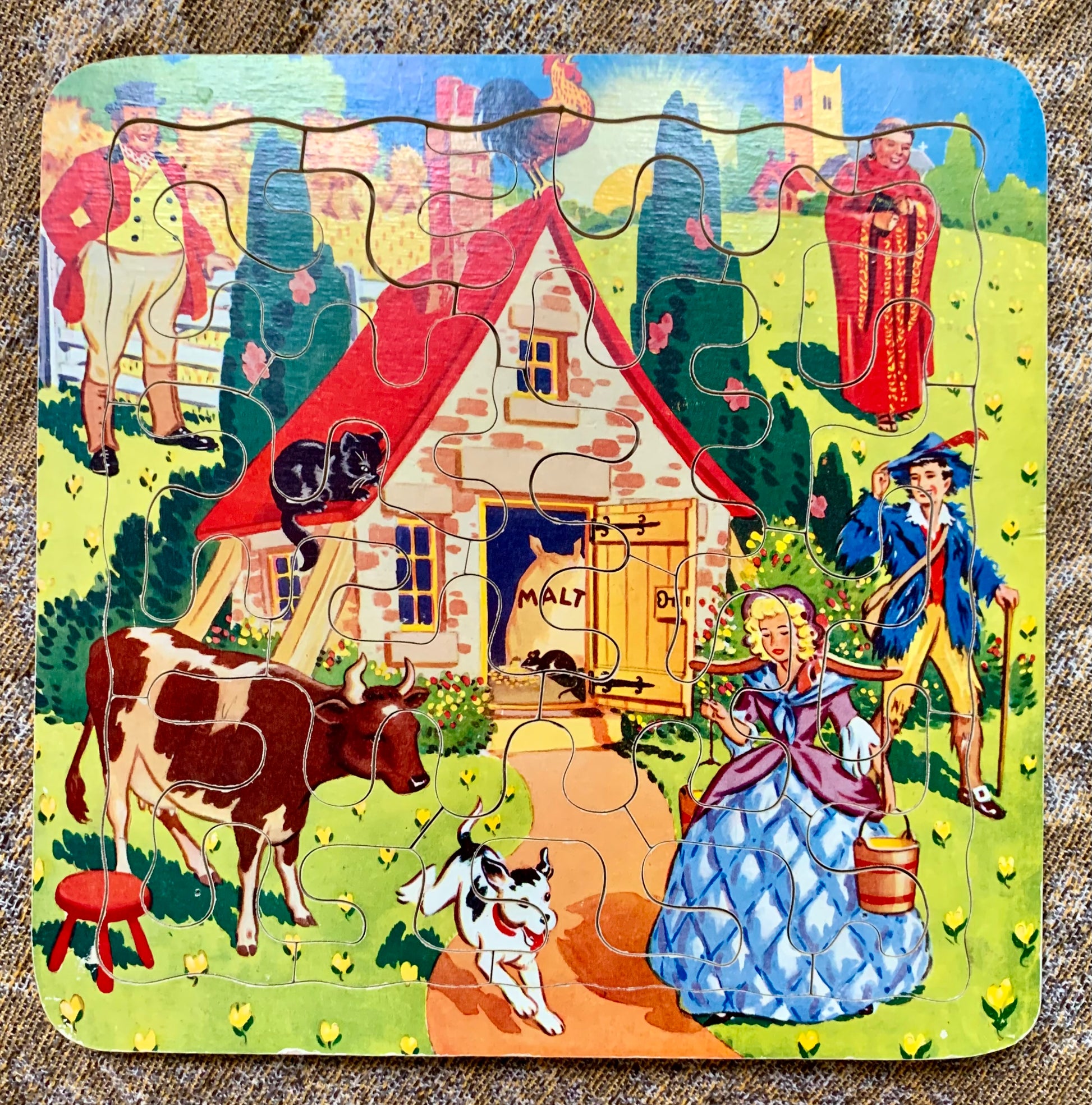 A square wooden jigsaw puzzle featuring a colorful vintage farm scene with a small house, cow, dog, people, and trees.
Photo by Karen King [image_link]
