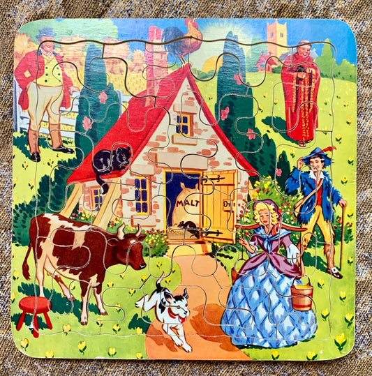 A square wooden jigsaw puzzle featuring a colorful vintage farm scene with a small house, cow, dog, people, and trees.
Photo by Karen King [image_link]