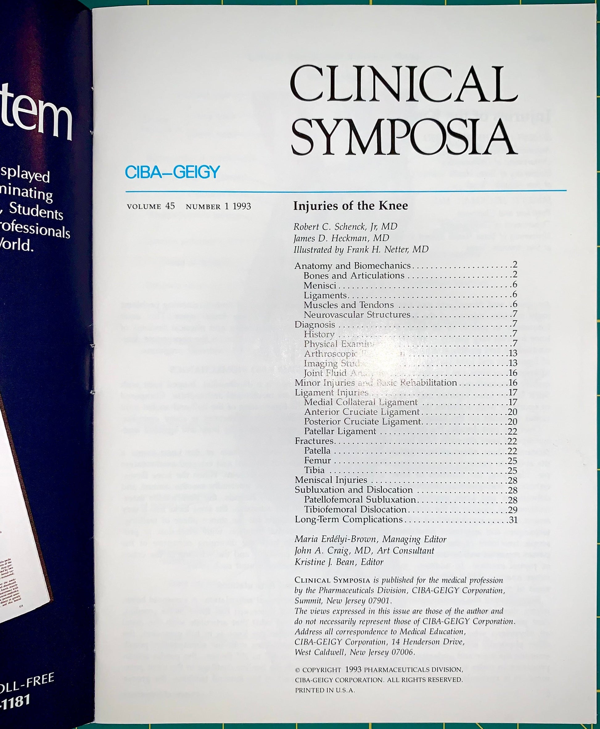 A printed book or magazine cover titled 'CLINICAL SYMPOSIA' with a table of contents for 'Injuries of the Knee.' The cover is photographed against a dark background, with part of another blue item visible at the left edge.
[additional_image_link]