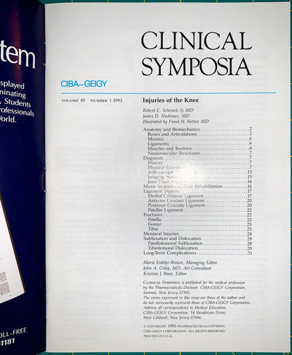 A printed book or magazine cover titled 'CLINICAL SYMPOSIA' with a table of contents for 'Injuries of the Knee.' The cover is photographed against a dark background, with part of another blue item visible at the left edge.
[additional_image_link]