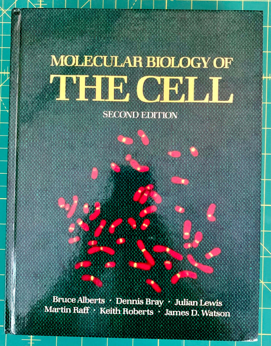 A hardcover textbook titled 'Molecular Biology of the Cell, Second Edition' with a dark textured cover, gold title text, and red cell illustrations, photographed on a green cutting mat.
[image_link]