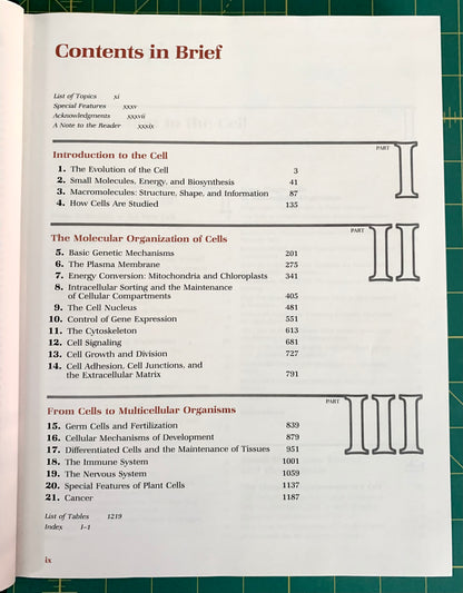 A printed table of contents page from a book or booklet titled 'Contents in Brief', photographed flat on a green grid cutting mat. The page is mostly white with black text and red headings, plus small red and blue section markers.
[additional_image_link]