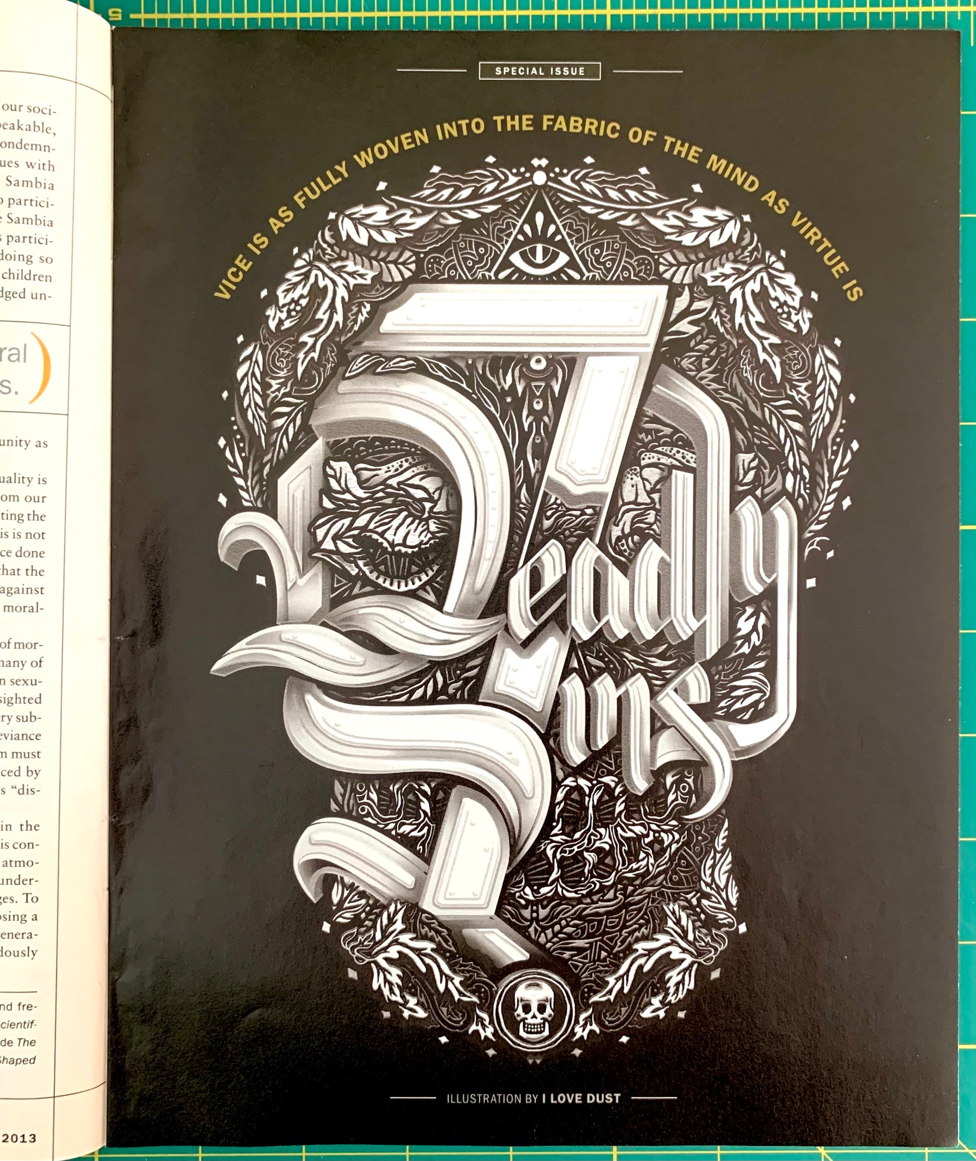A black book or booklet spread showing a large ornate silver illustration reading 'Deadly Vices' with decorative typography, a skull motif, and surrounding text. The left page is partially visible and the item is photographed on a green cutting mat.
[additional_image_link]