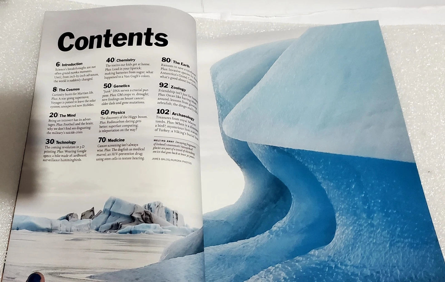 An open printed booklet or magazine spread showing a table of contents on the left page and a large icy blue landscape photograph on the right page, photographed on a white textured surface.
[additional_image_link]
