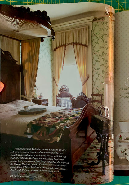 A printed interior design page or magazine spread showing a large bedroom scene with a dark wood four-poster, patterned bedding, curtains, and wallpaper, alongside a side view of a matching bed frame. A hand is visible holding the page, and the page is photographed against a green cutting mat.
[additional_image_link]