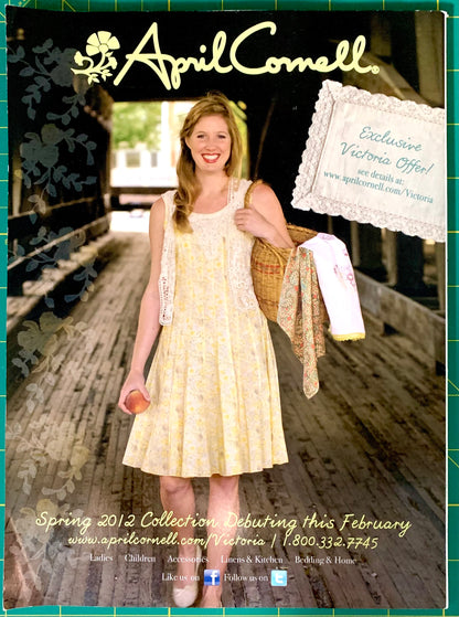 A promotional catalog-style image featuring a smiling woman wearing a pale yellow floral sleeveless dress while standing on a wooden walkway. The image includes the April Cornell brand name at the top, a lace sample tag on the right, and collection text at the bottom.
[additional_image_link]