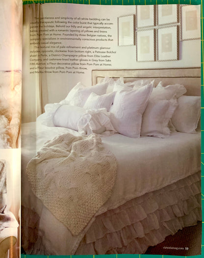 An open magazine or catalog page showing a styled bed with white bedding, multiple pillows, and a textured throw blanket. The page includes a block of text on the left and a green border around the photo.
[additional_image_link]