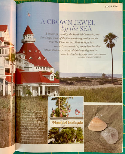 An open printed magazine or book spread showing a travel page about Hotel del Caronado in Santa Cruz, with a large photo of the red-roofed building, beach scenery, and a small inset photo of seashells on sand. The page is photographed against a green grid background.
[additional_image_link]