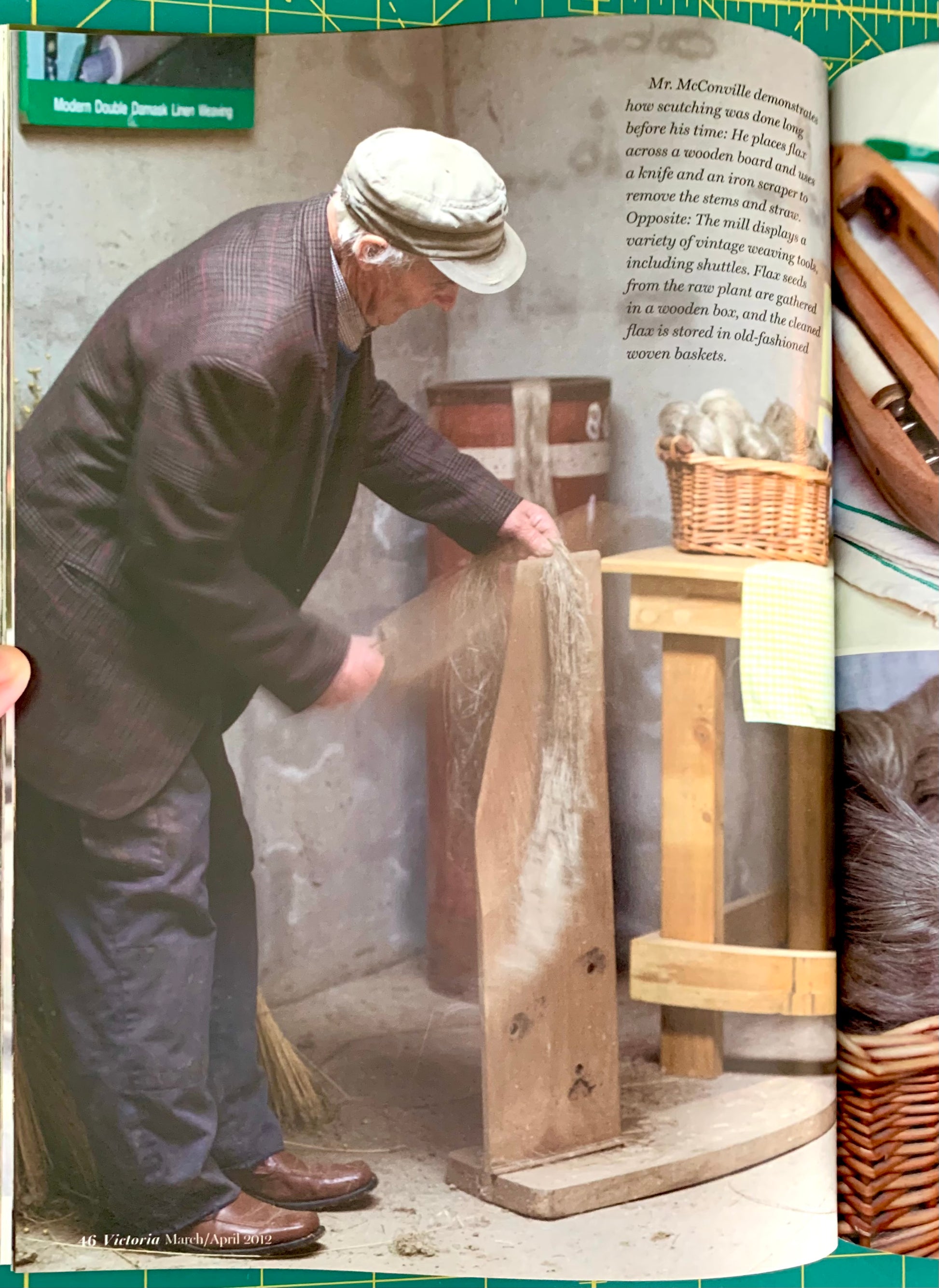 A printed magazine or book page showing a man in a dark suit and cap working at a wooden bench, with a large inset photo of a close-up of a brown textured material on the right side. The page has a green cutting mat border around it.
[additional_image_link]