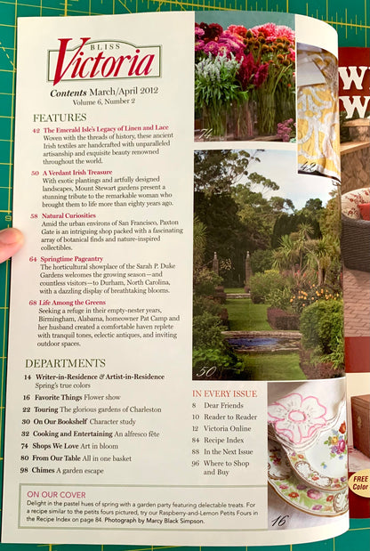 A hand holding a printed magazine or book page featuring the Victoria recipe collection, with a floral kitchen scene printed on the right page and visible text sections like Features and Departments.
[additional_image_link]