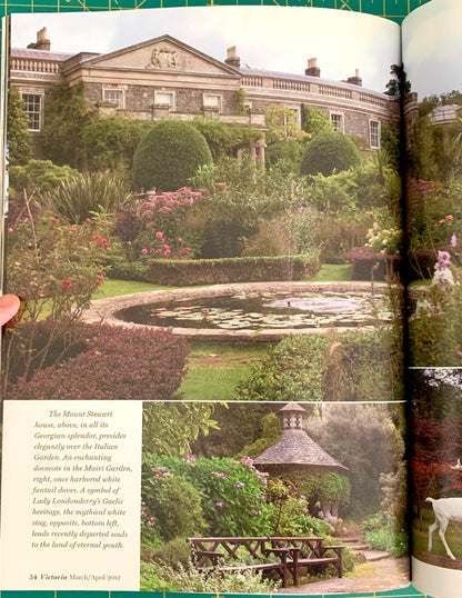 An open book showing a printed page with a large photograph of a formal garden and stone mansion, plus smaller inset photos and a block of text. A hand is holding the left edge of the book.
[additional_image_link]