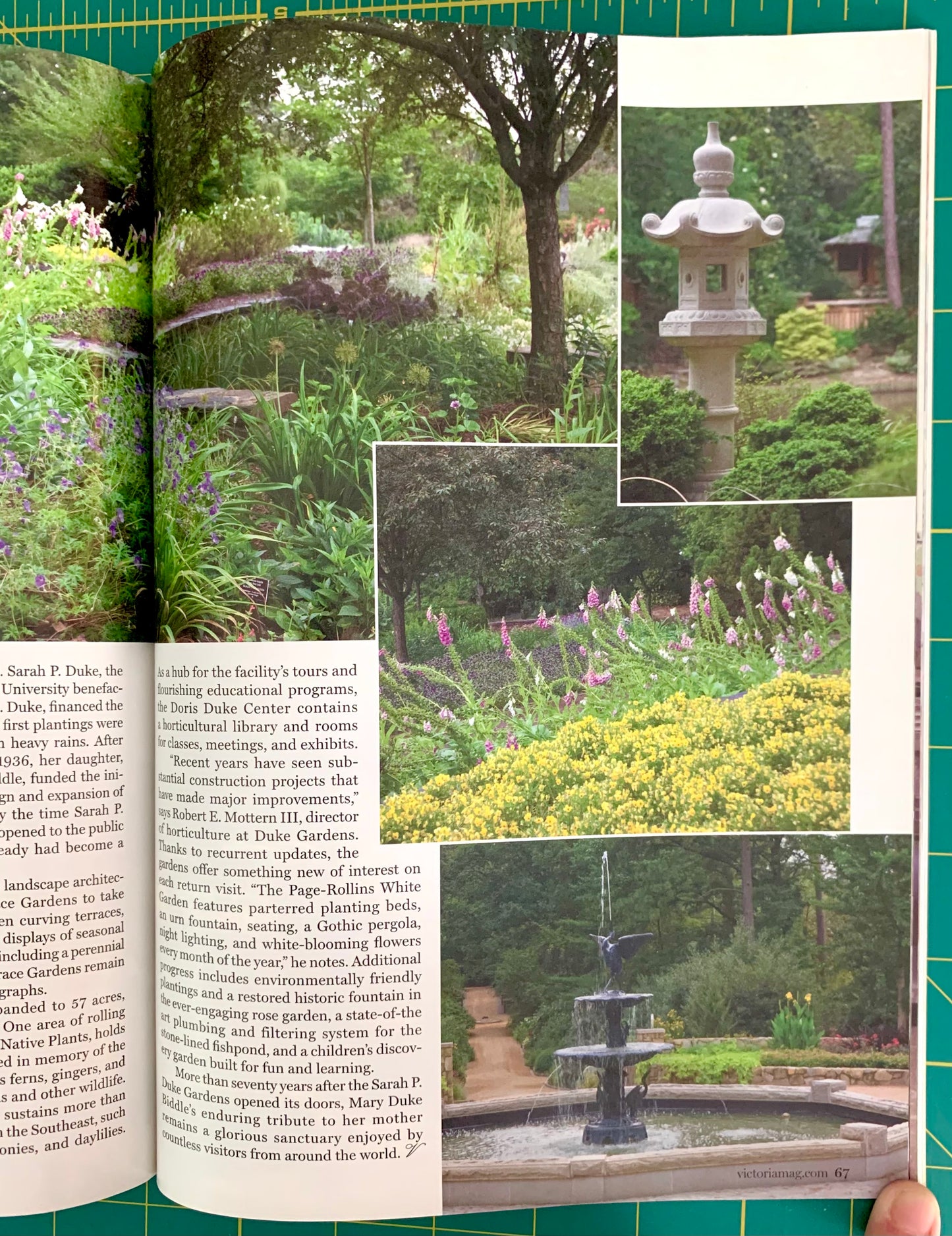 An open book showing a garden landscape photograph with text columns and inset photos of a stone lantern and flowering plants, photographed on a green cutting mat with a finger visible at the bottom right.
[additional_image_link]
