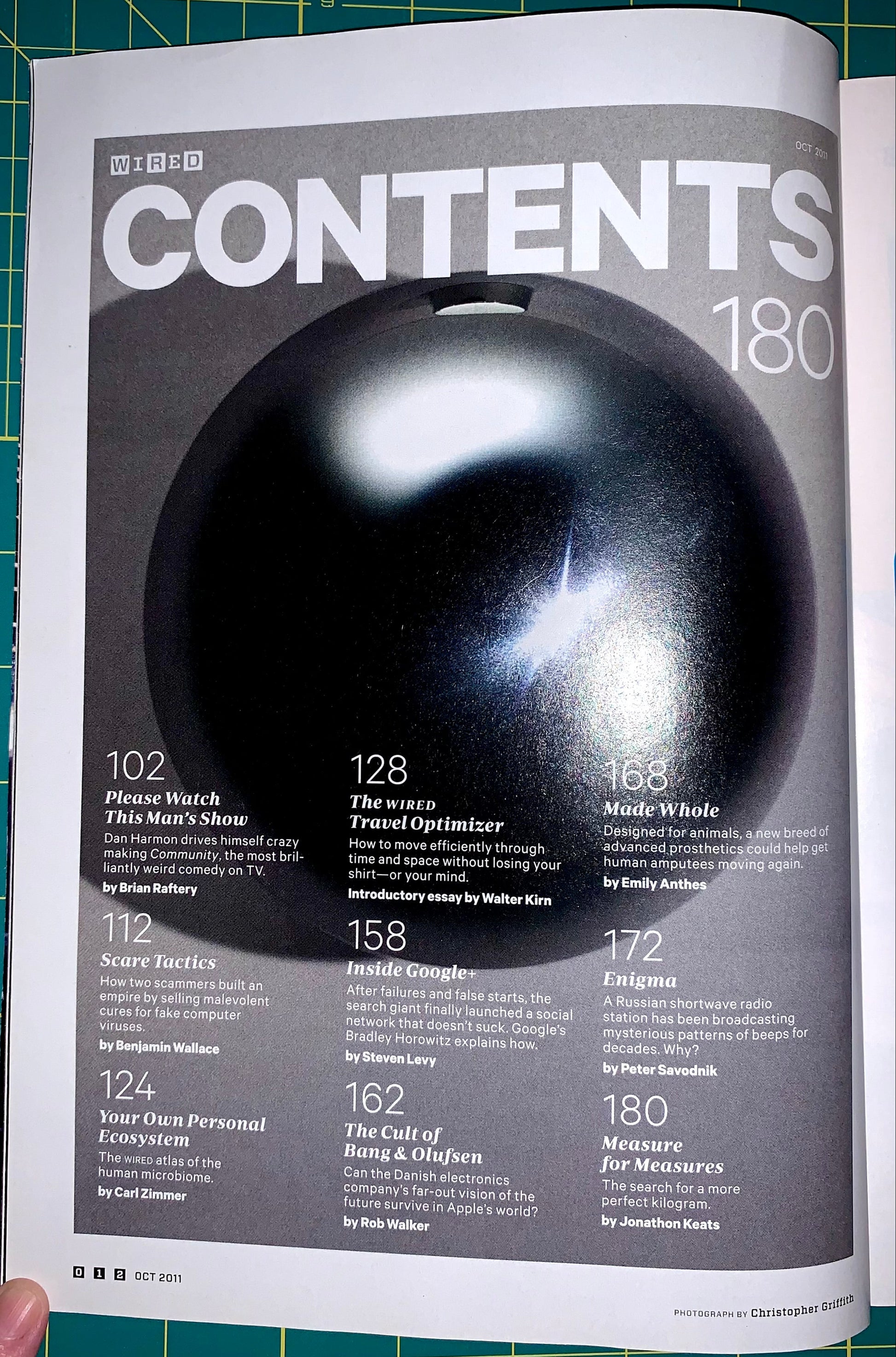 A printed magazine or book page featuring a large glossy black sphere on a gray background with the title 'BBC CONTENTS 180' and multiple text callouts around it. A hand is partially visible at the bottom left, and the page is photographed on a green cutting mat.
[additional_image_link]