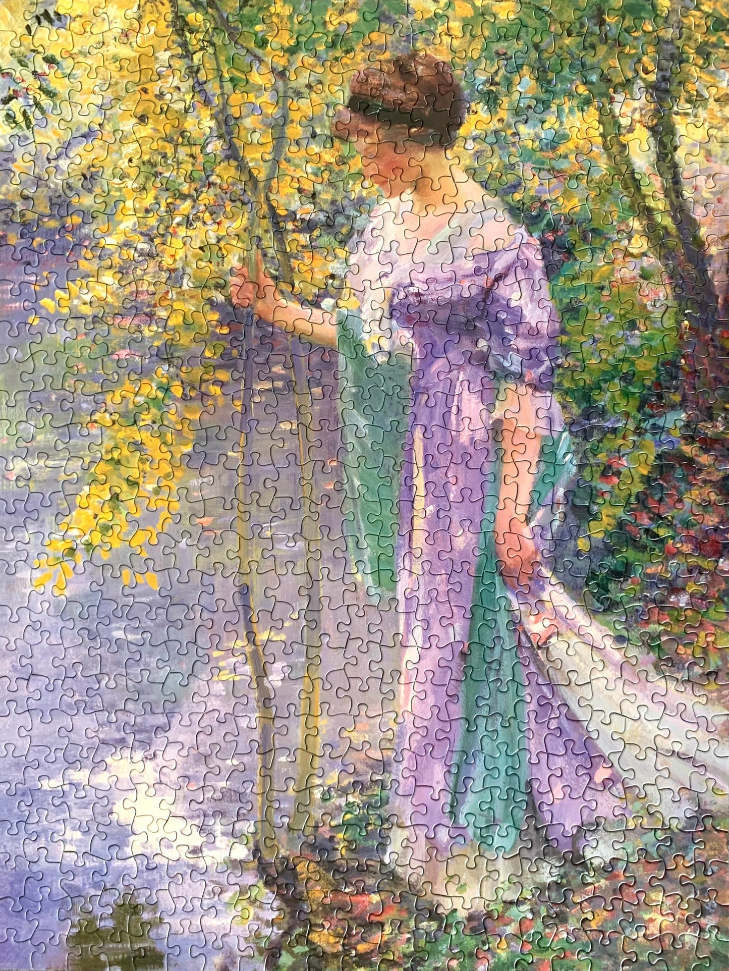 A jigsaw puzzle depicting a woman in a purple dress standing at a water's edge in a garden setting, with green and yellow colors in the background.
Photo by Karen King [additional_image_link]